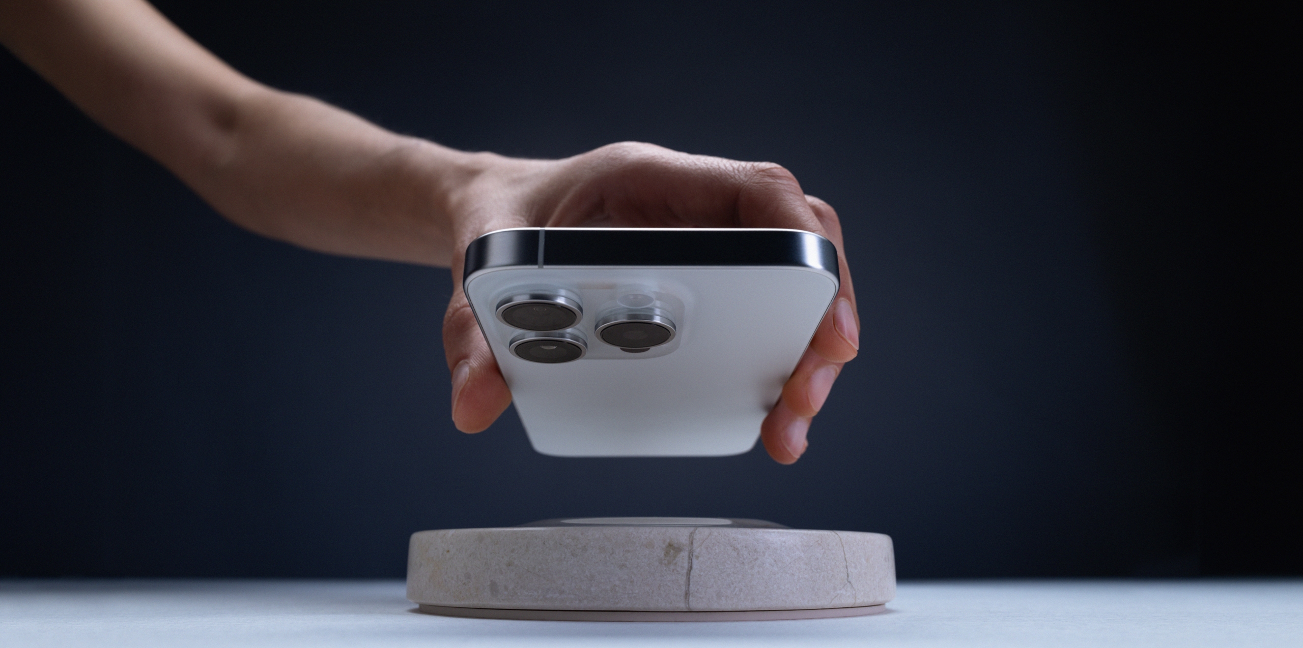 A person holds a Qi-enabled smartphone over a cream marble Classic Stone wireless charging pad.